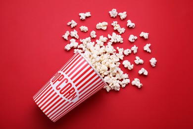 Photo of Overturned paper cup with delicious popcorn on red background, flat lay