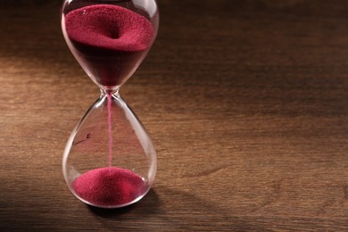 Photo of Hourglass with pink flowing sand on wooden table. Space for text