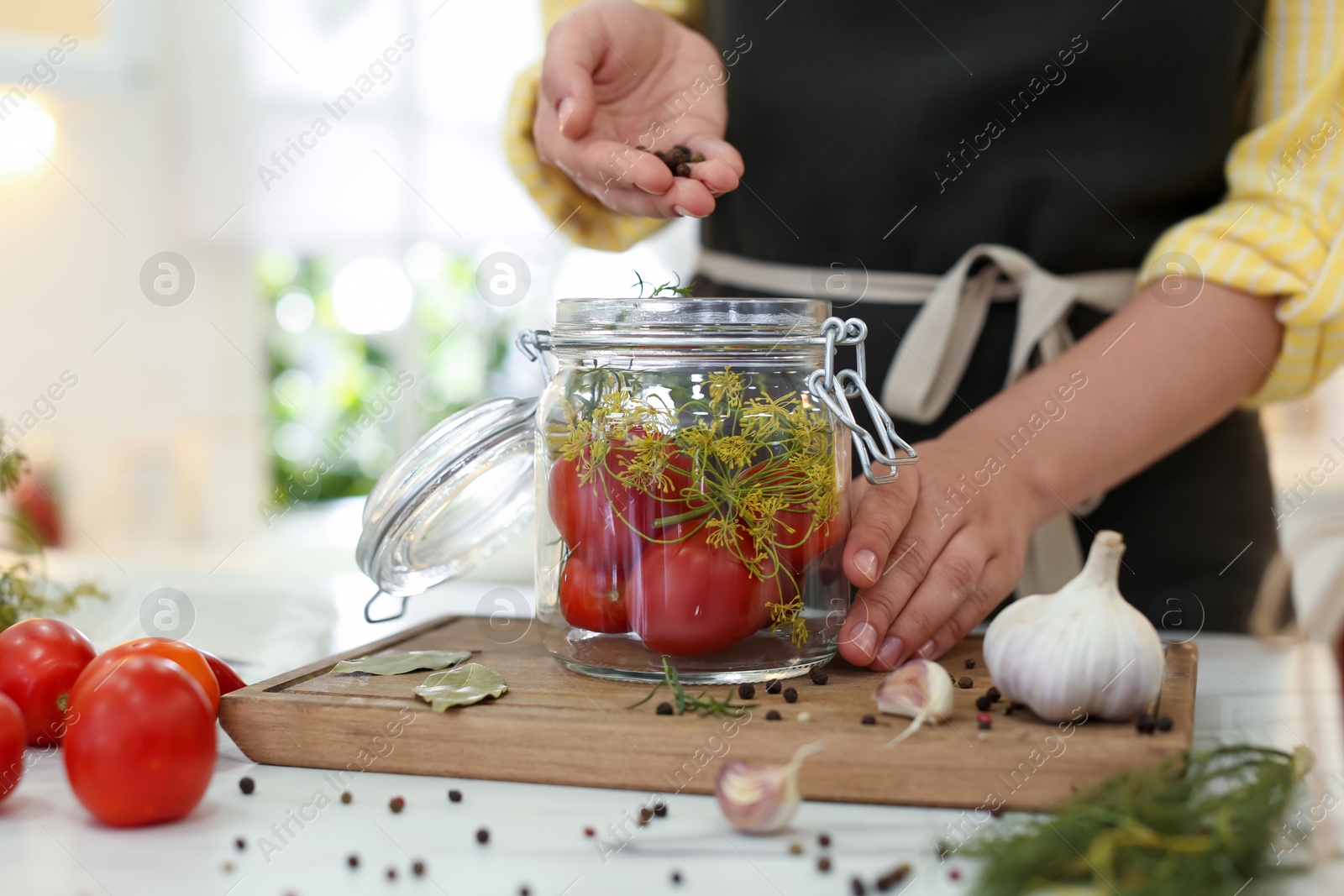 Photo of Woman putting peppercorns into pickling jar at kitchen table, closeup