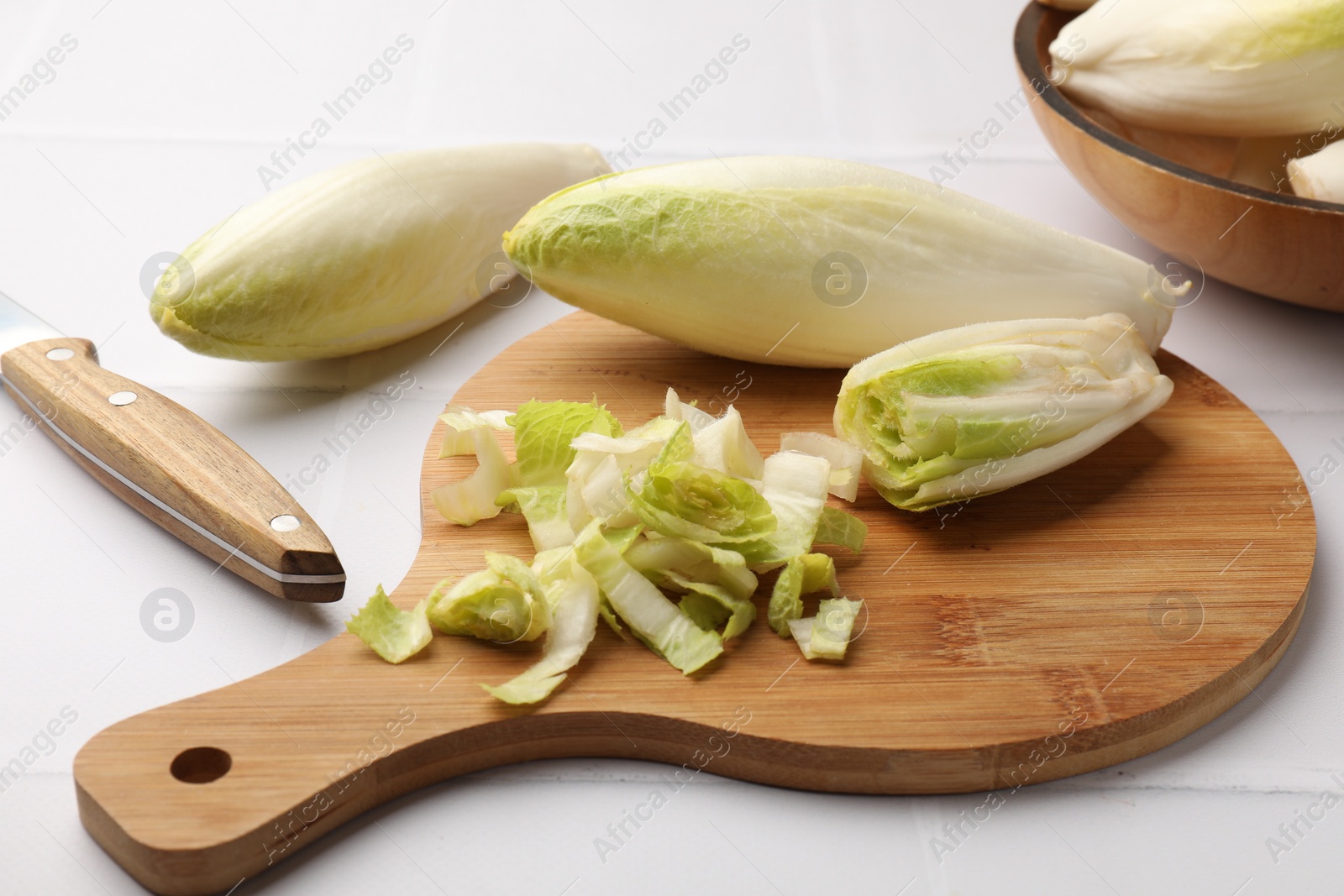 Photo of Fresh raw Belgian endives (chicory), wooden board and knife on white tiled table