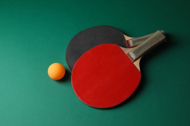 Photo of Ping pong ball and rackets on green background, flat lay