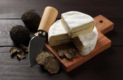 Photo of Delicious cheese, fresh black truffles and knife on wooden table