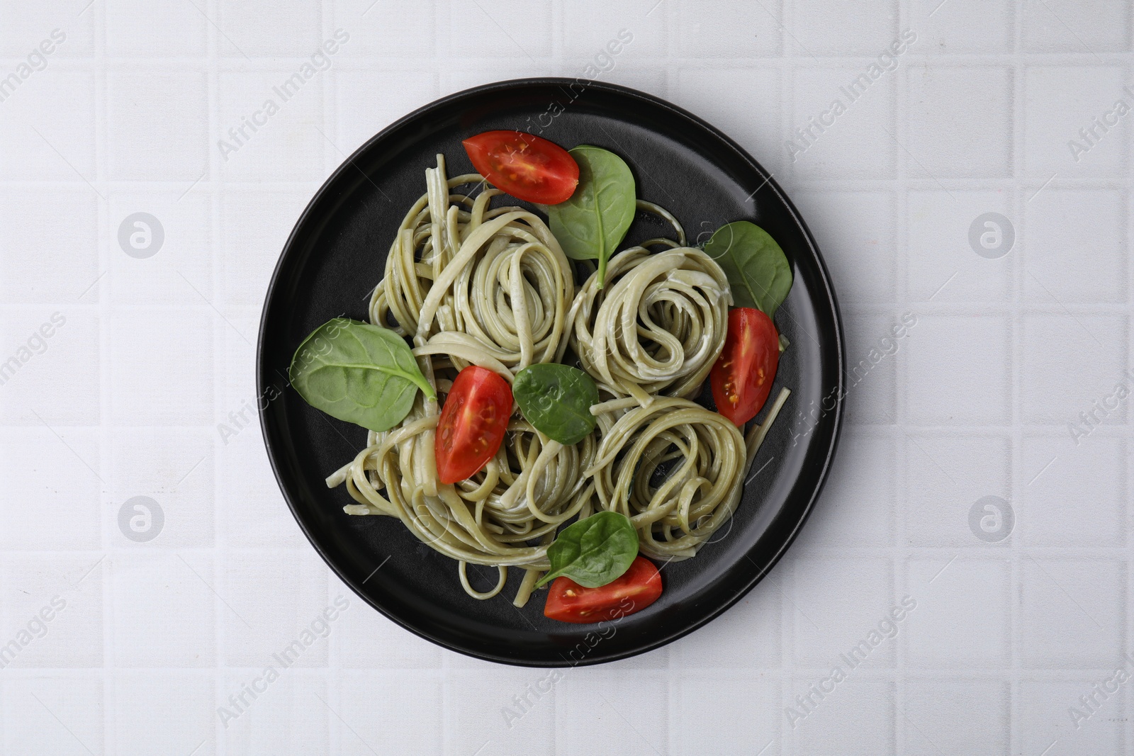 Photo of Tasty pasta with spinach, sauce and tomatoes on white tiled table, top view