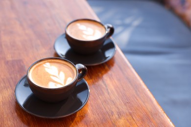 Photo of Cups of aromatic coffee with foam on wooden table in outdoor cafe. Space for text