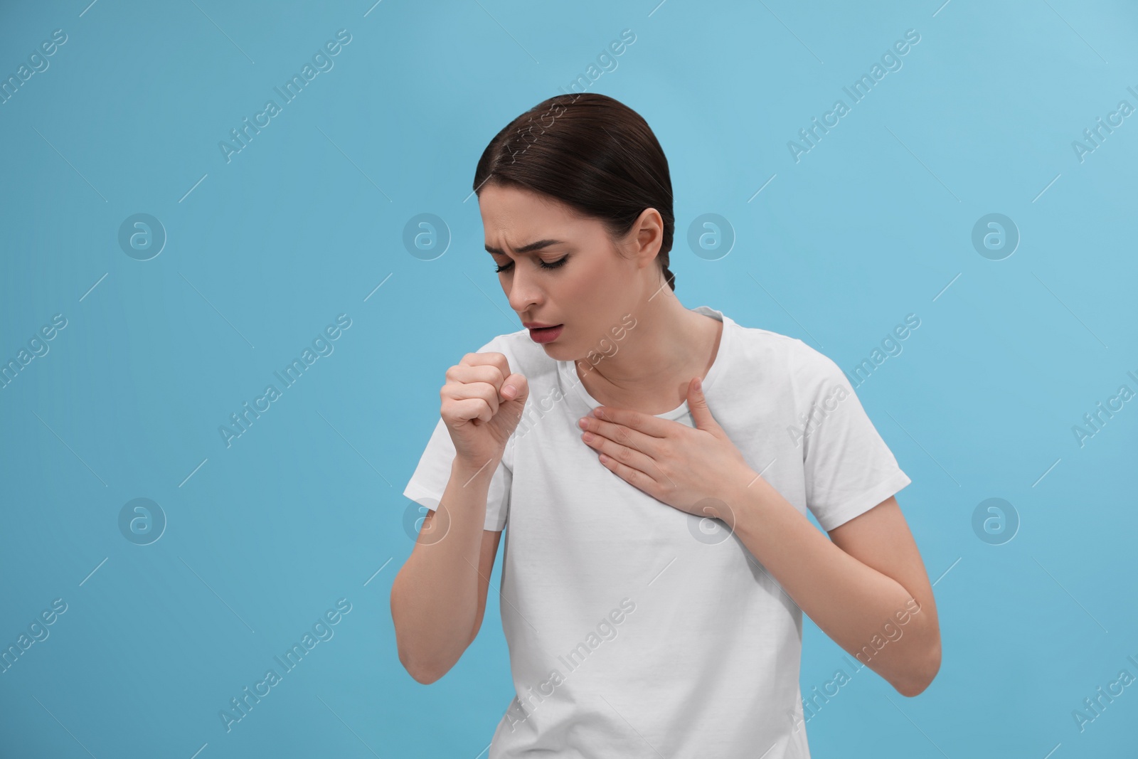 Photo of Woman coughing on light blue background. Cold symptoms