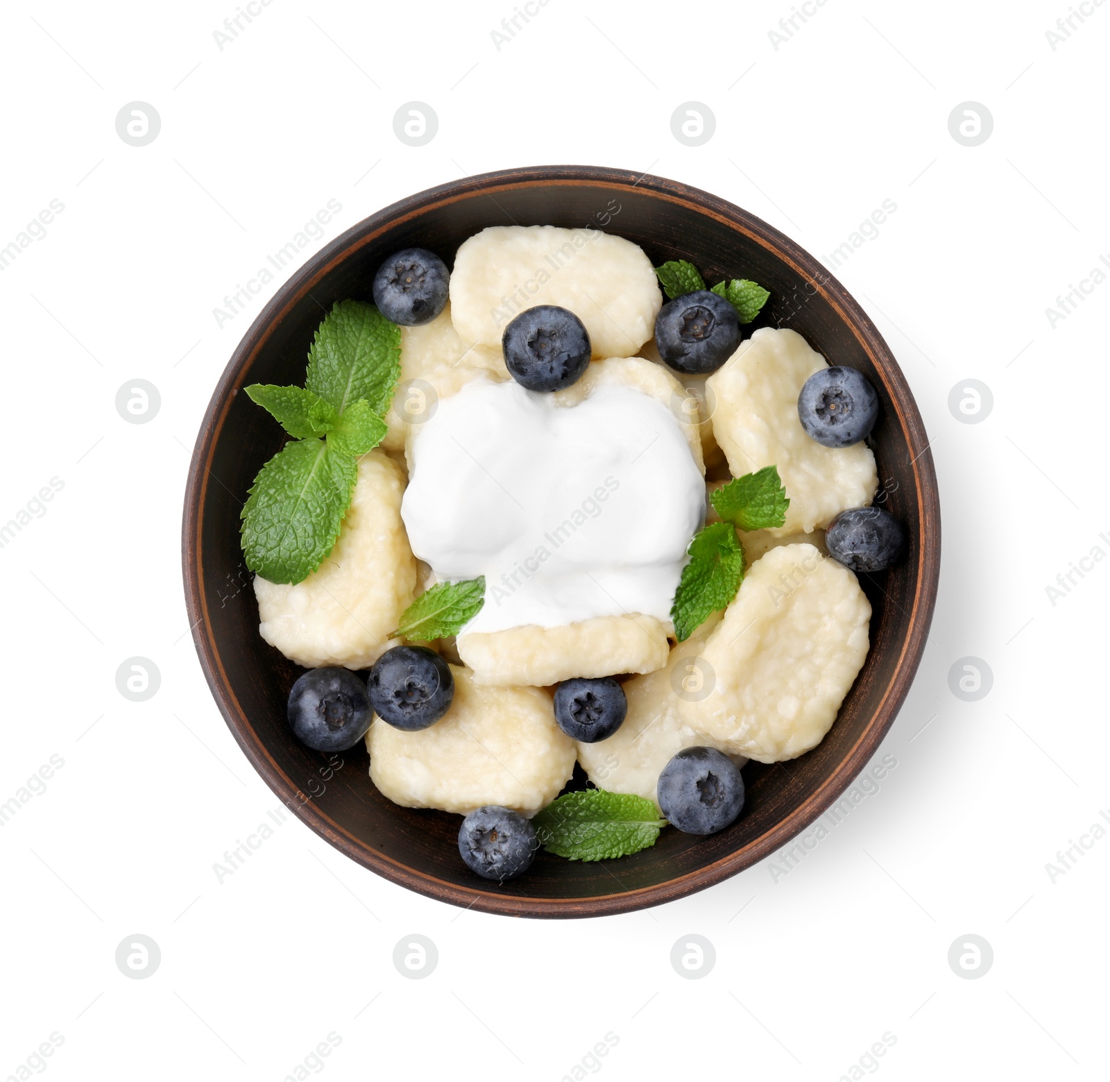 Photo of Bowl of tasty lazy dumplings with blueberries, mint leaves and sour cream isolated on white, top view