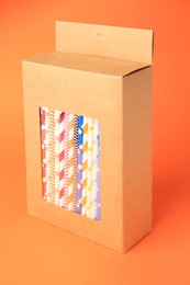 Box with many paper drinking straws on orange background