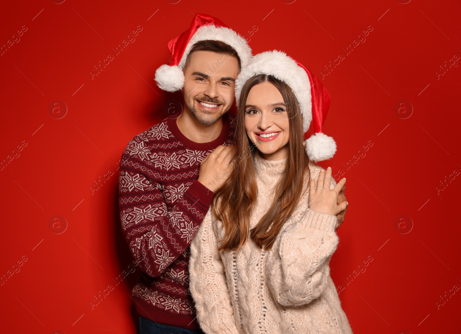 Photo of Couple wearing Christmas sweaters and Santa hats on red background