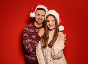 Couple wearing Christmas sweaters and Santa hats on red background