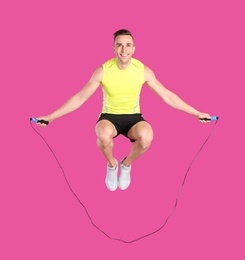 Full length portrait of young sportive man training with jump rope on color background