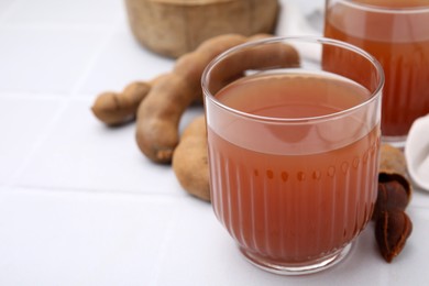 Photo of Glass of refreshing tamarind drink and fresh fruits on white table, closeup. Space for text