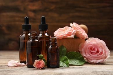 Photo of Bottles of rose essential oil and flowers on wooden table, space for text