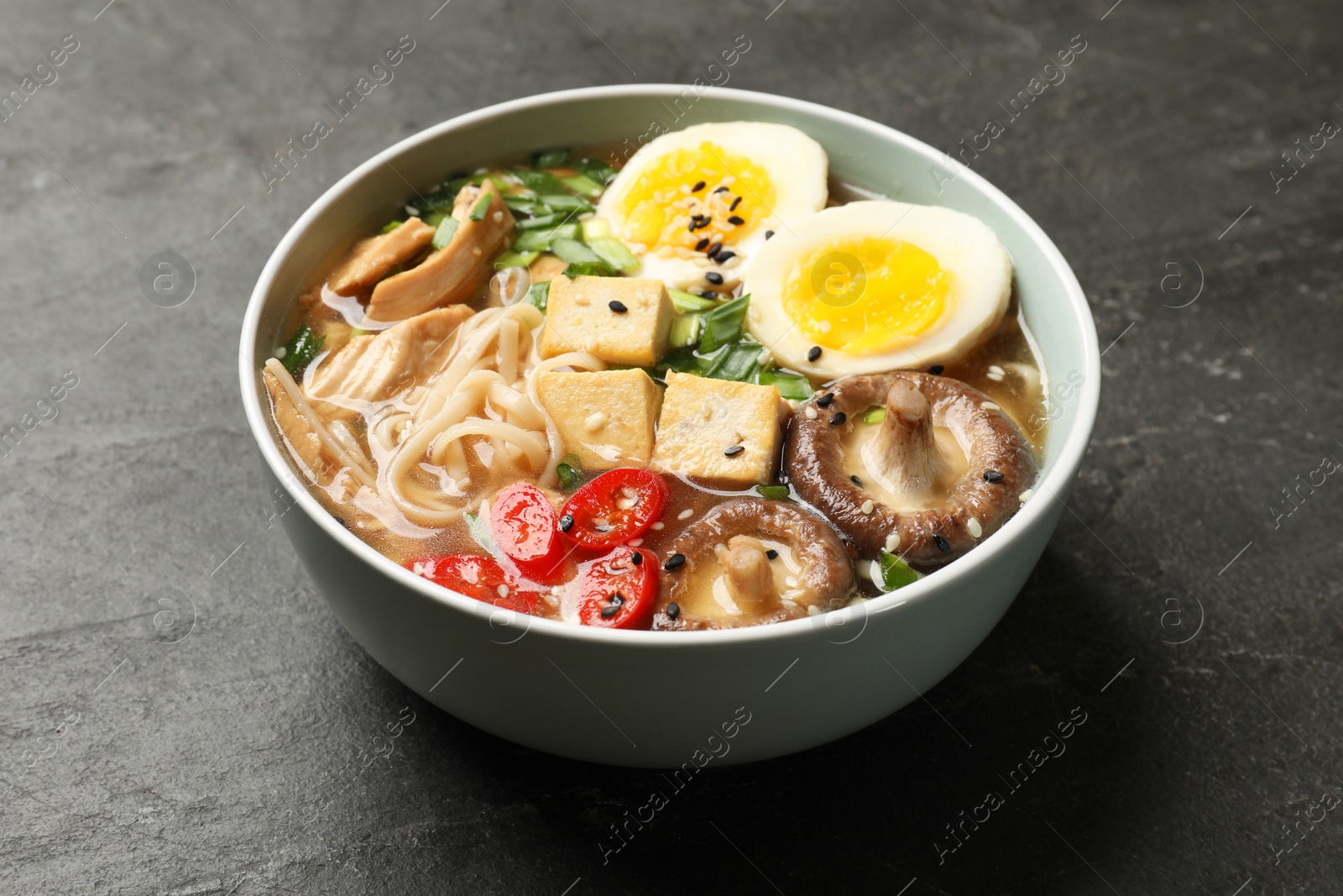 Photo of Noodle soup. Bowl of delicious ramen on black table, closeup