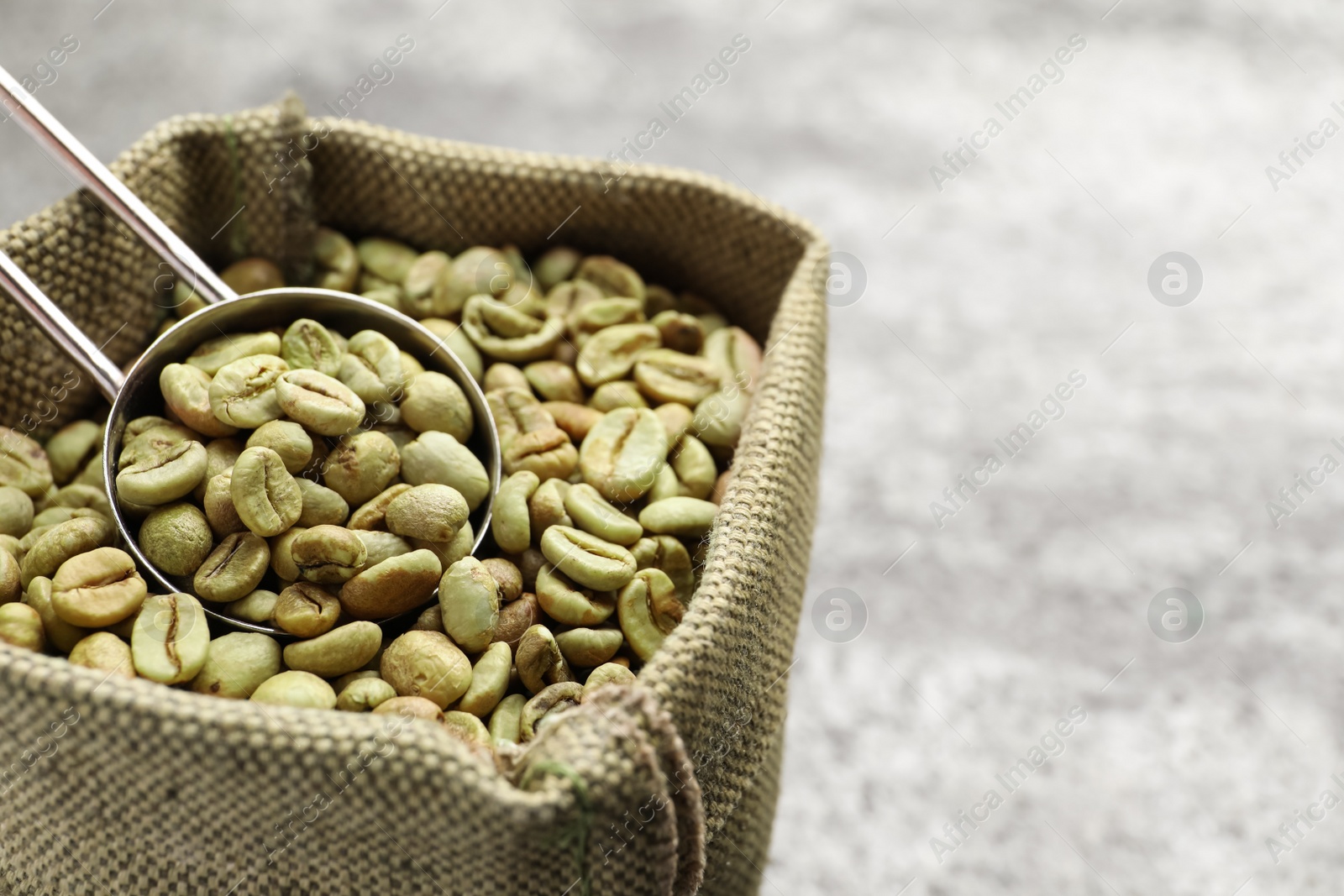 Photo of Green coffee beans and scoop in sackcloth bag on table, closeup. Space for text