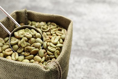 Photo of Green coffee beans and scoop in sackcloth bag on table, closeup. Space for text