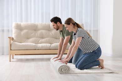 Smiling couple unrolling carpet with beautiful pattern on floor in room. Space for text