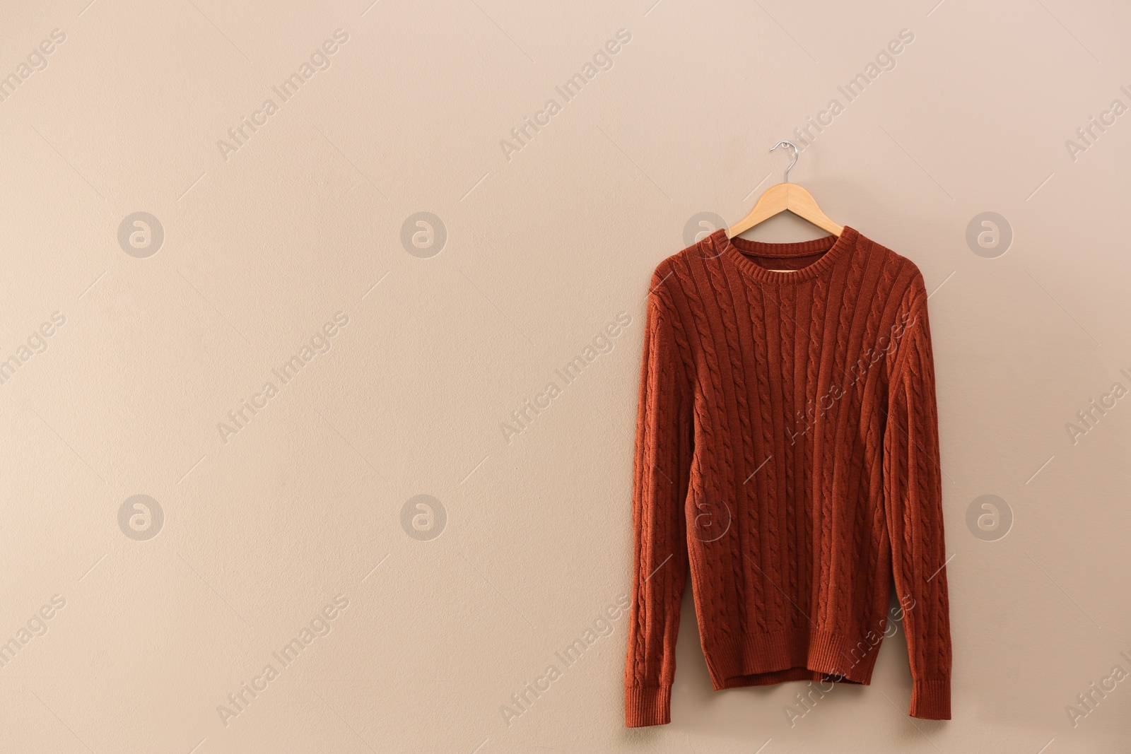 Photo of Hanger with stylish sweater on beige wall. Space for text