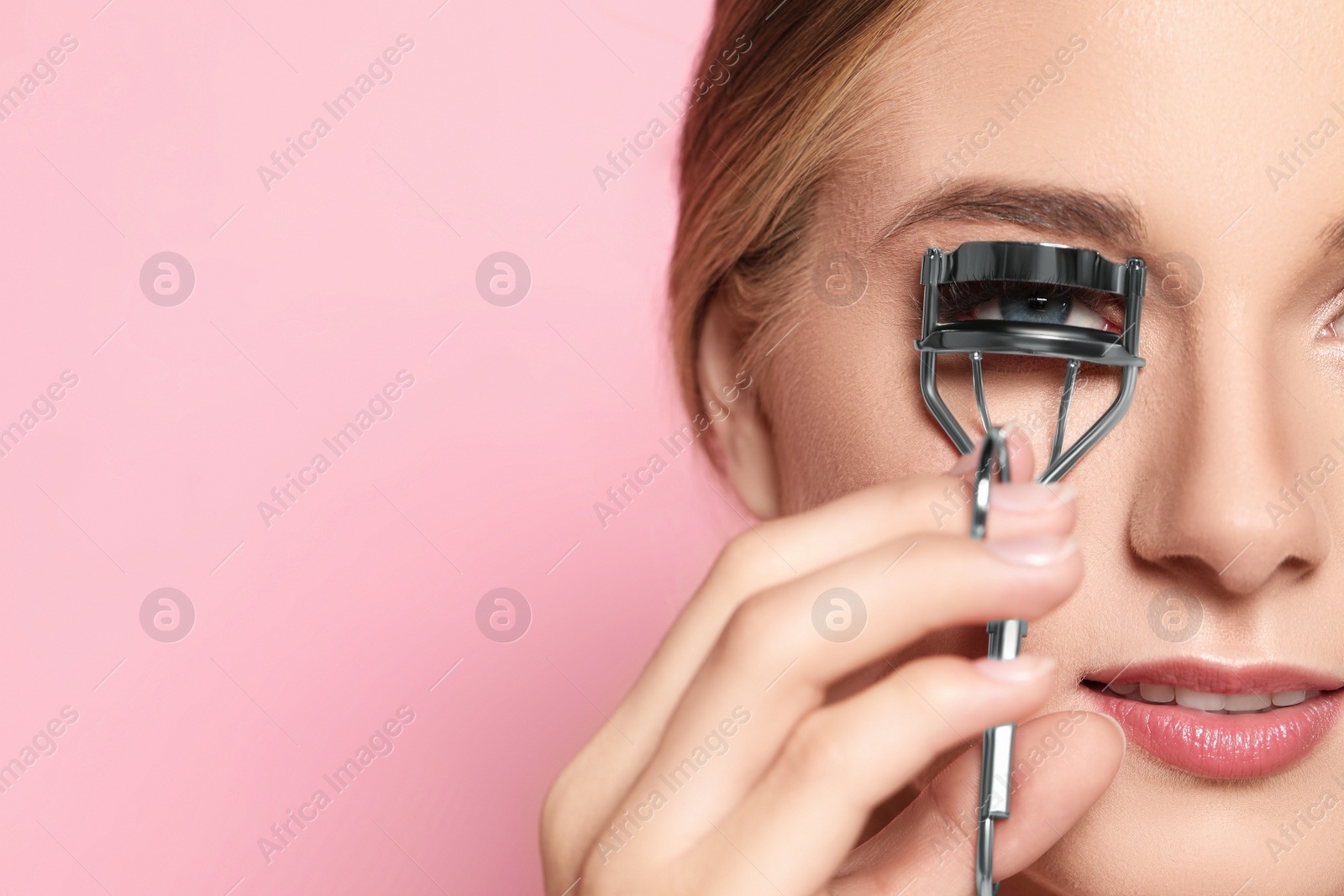 Photo of Young woman using eyelash curler on pink background, closeup. Space for text