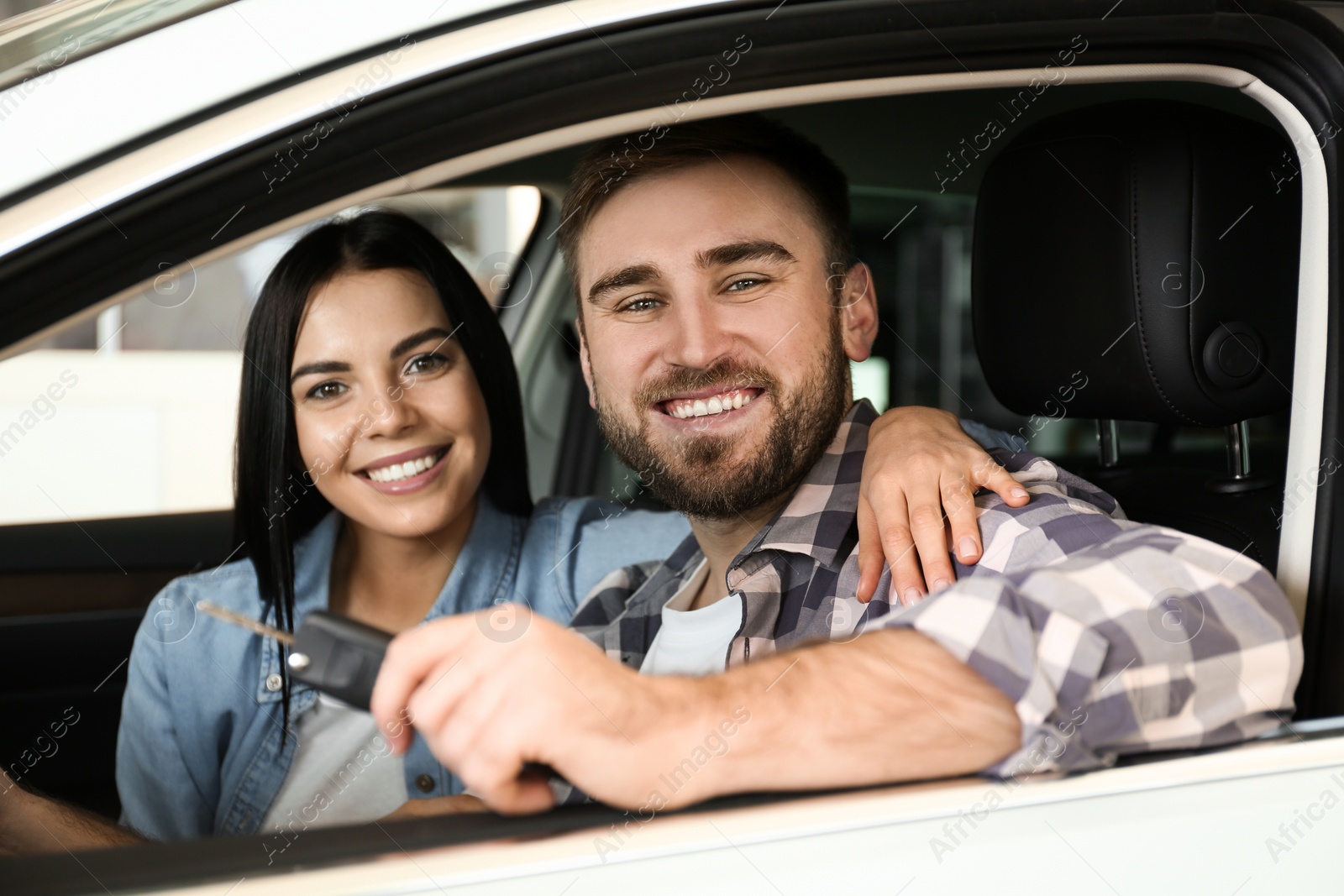 Photo of Happy couple with car key sitting in modern auto at dealership