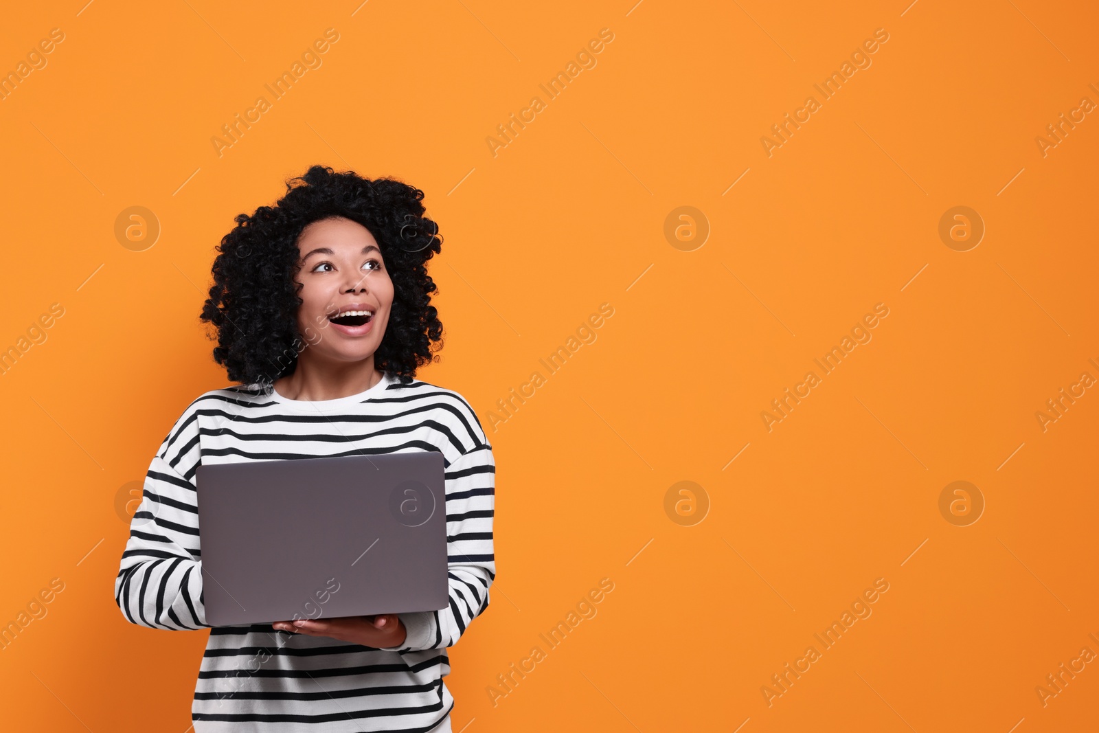 Photo of Happy young woman with laptop on orange background. Space for text