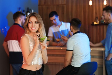 Beautiful young woman with glass of martini cocktail in bar