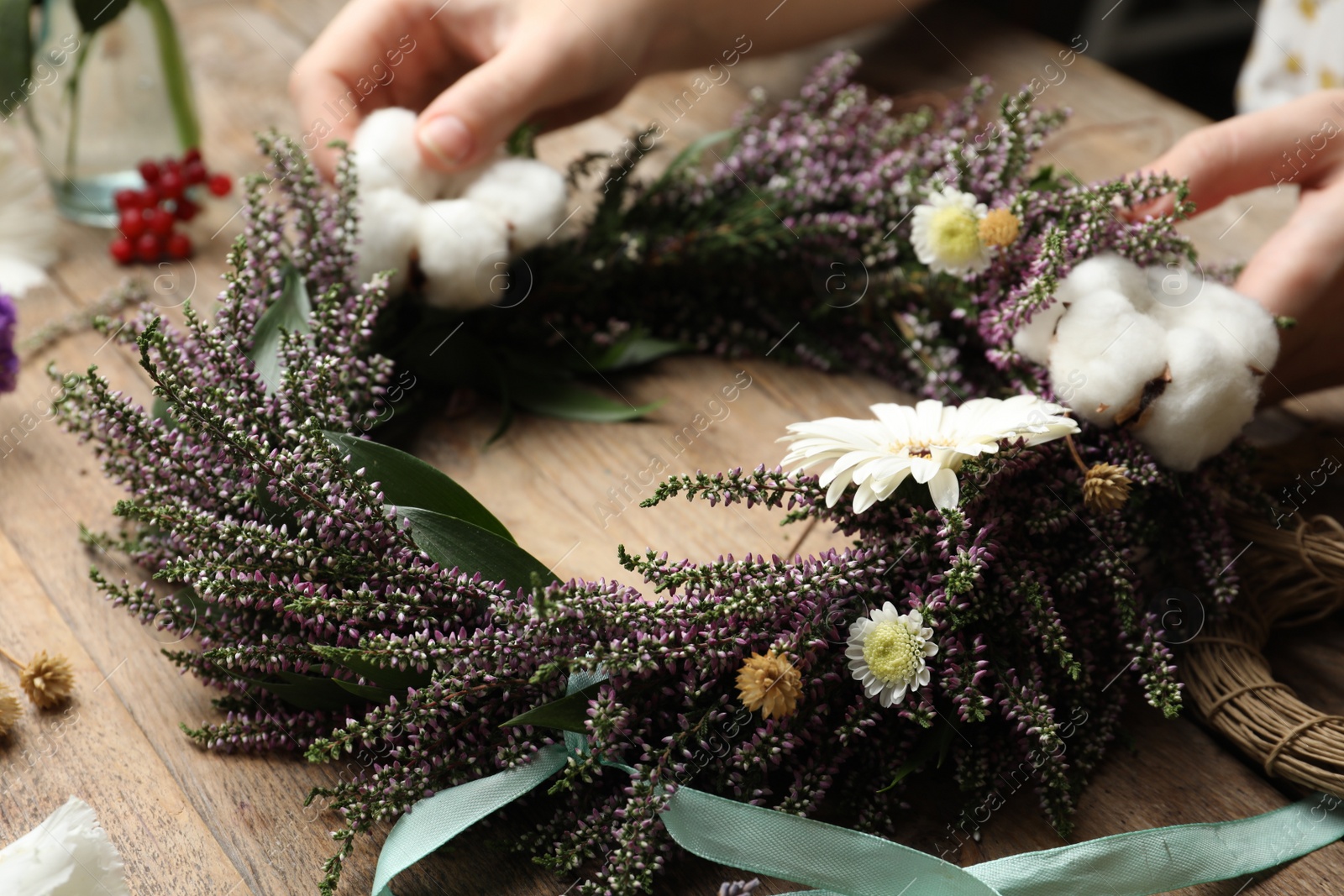 Photo of Florist making beautiful autumnal wreath with heather flowers at wooden table, closeup