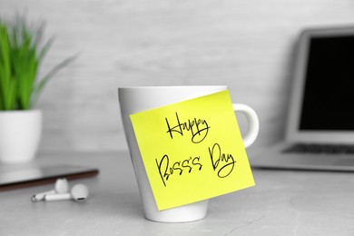 Image of Sticky note with phrase Happy Boss`s Day attached to cup on grey table in office
