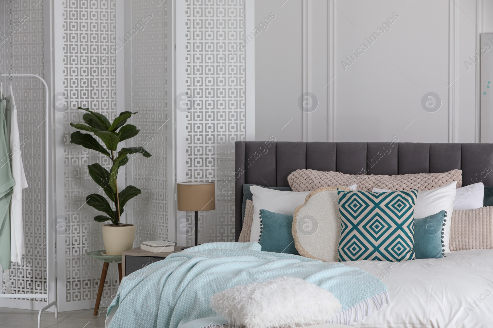 Photo of Stylish light bedroom interior with large comfortable bed, houseplant and folding screen