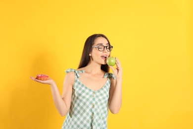Photo of Concept of choice. Woman eating apple and holding doughnut on yellow background