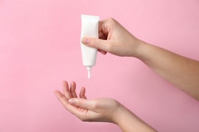 Photo of Woman applying cosmetic cream from tube onto her hand on pink background, closeup