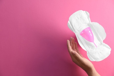 Woman holding hand near menstrual pad and cup on color background, top view. Gynecological care