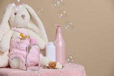 Photo of Baby cosmetic products, toy bunny, accessories and soap bubbles on beige background. Space for text