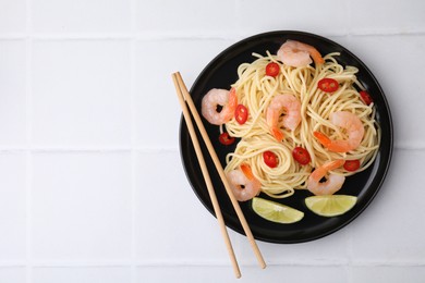 Tasty spaghetti with shrimps, chili pepper and lime on light tiled table, top view. Space for text