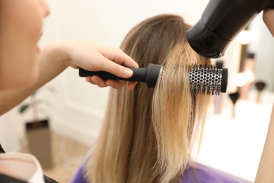 Photo of Stylist drying client's hair in beauty salon, closeup