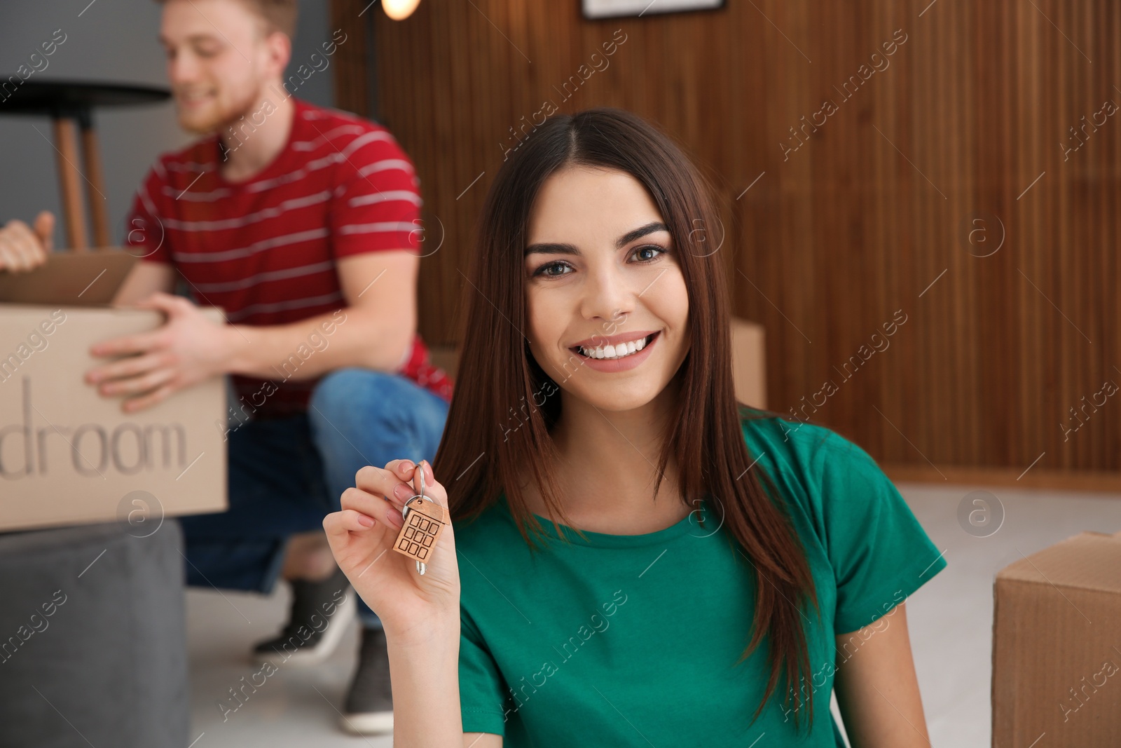 Photo of Young woman with key from new house and her boyfriend indoors. Moving day