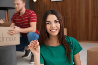 Young woman with key from new house and her boyfriend indoors. Moving day