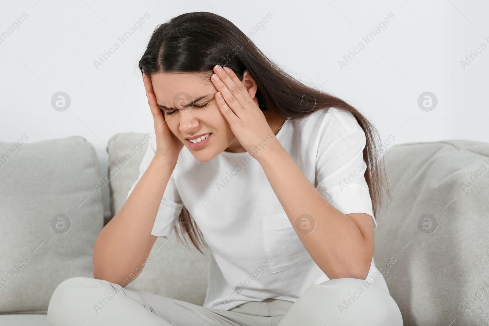 Photo of Young woman suffering from headache on sofa indoors. Hormonal disorders