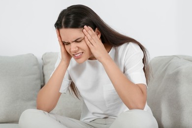 Photo of Young woman suffering from headache on sofa indoors. Hormonal disorders