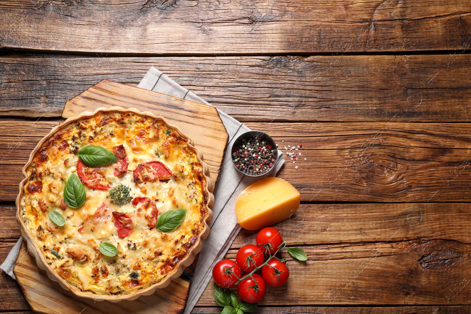 Photo of Tasty quiche with tomatoes, basil and cheese served on wooden table, flat lay. Space for text