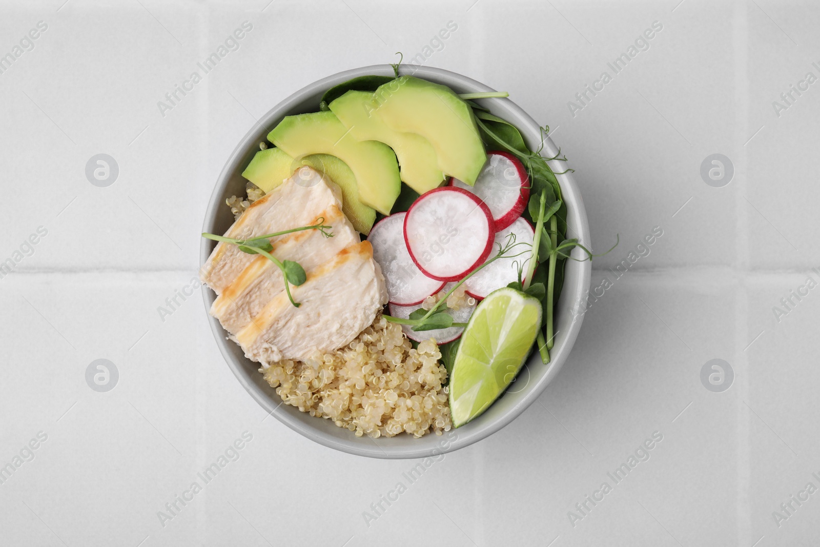 Photo of Delicious quinoa salad with chicken, avocado and radish on white tiled table, top view