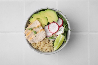 Delicious quinoa salad with chicken, avocado and radish on white tiled table, top view