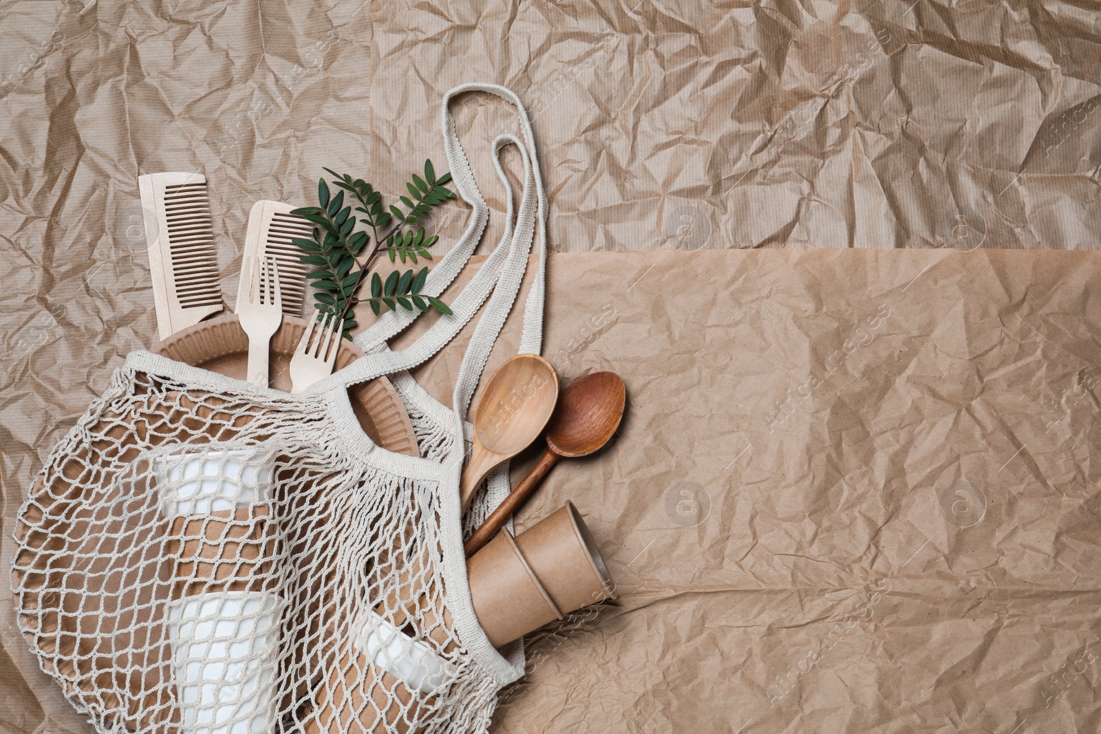 Photo of Net bag with different eco items on crumpled paper, top view and space for text. Recycling concept