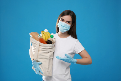 Female volunteer in protective mask and gloves with products on blue background. Aid during coronavirus quarantine