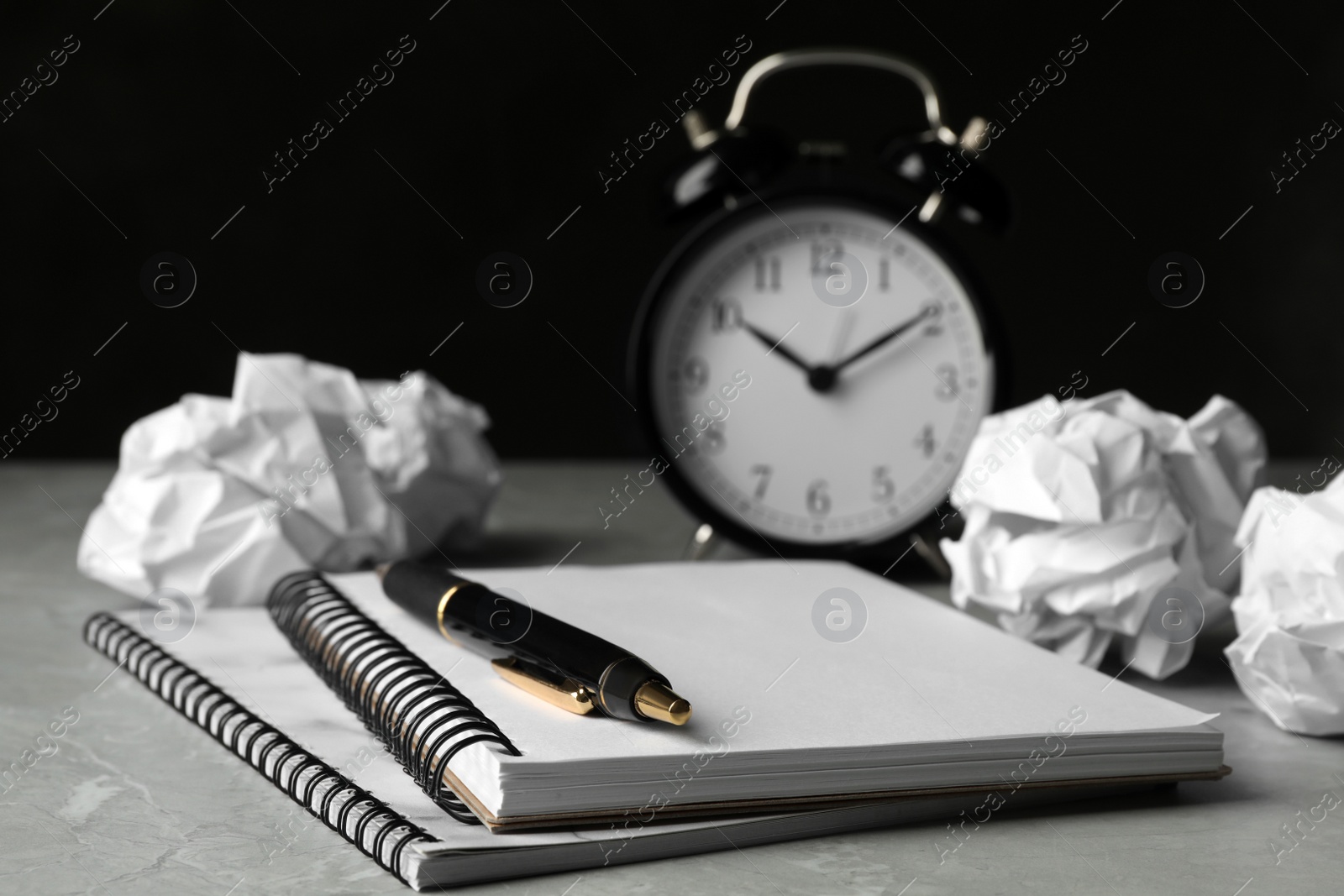 Photo of Notebooks, crumpled paper balls and alarm clock on grey table