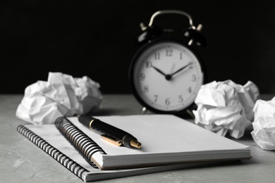 Notebooks, crumpled paper balls and alarm clock on grey table