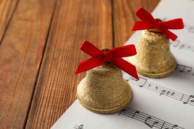 Photo of Golden shiny bells with red bows and music sheet on wooden table, closeup. Space for text. Christmas decoration