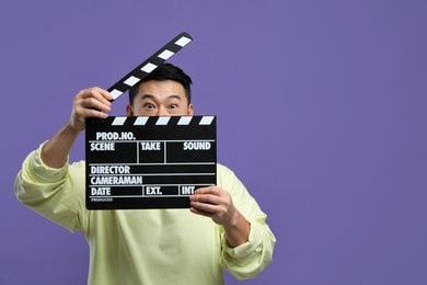 Emotional asian actor with clapperboard on purple background, space for text. Film industry