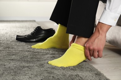 Photo of Man putting on yellow socks indoors, closeup