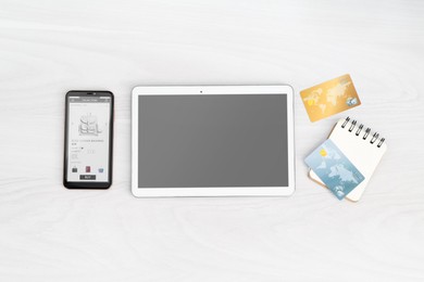 Online store website on device screen. Tablet, smartphone, notebook and credit cards on white wooden table, flat lay