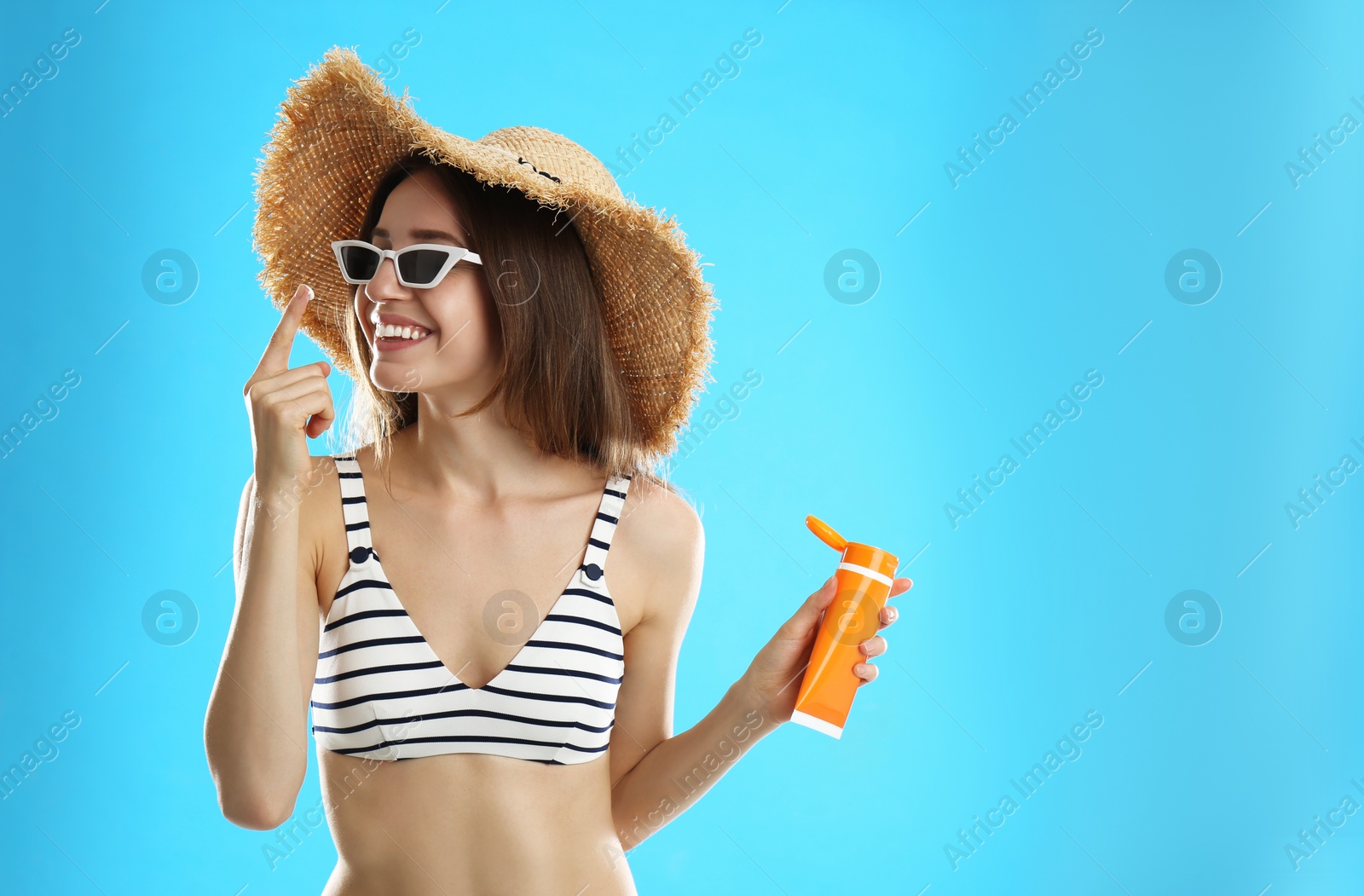 Photo of Young woman applying sun protection cream on light blue background. Space for text